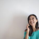 portrait photo of smiling woman in a teal top talking on the phone