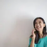 portrait photo of smiling woman in a teal top talking on the phone