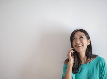 portrait photo of smiling woman in a teal top talking on the phone